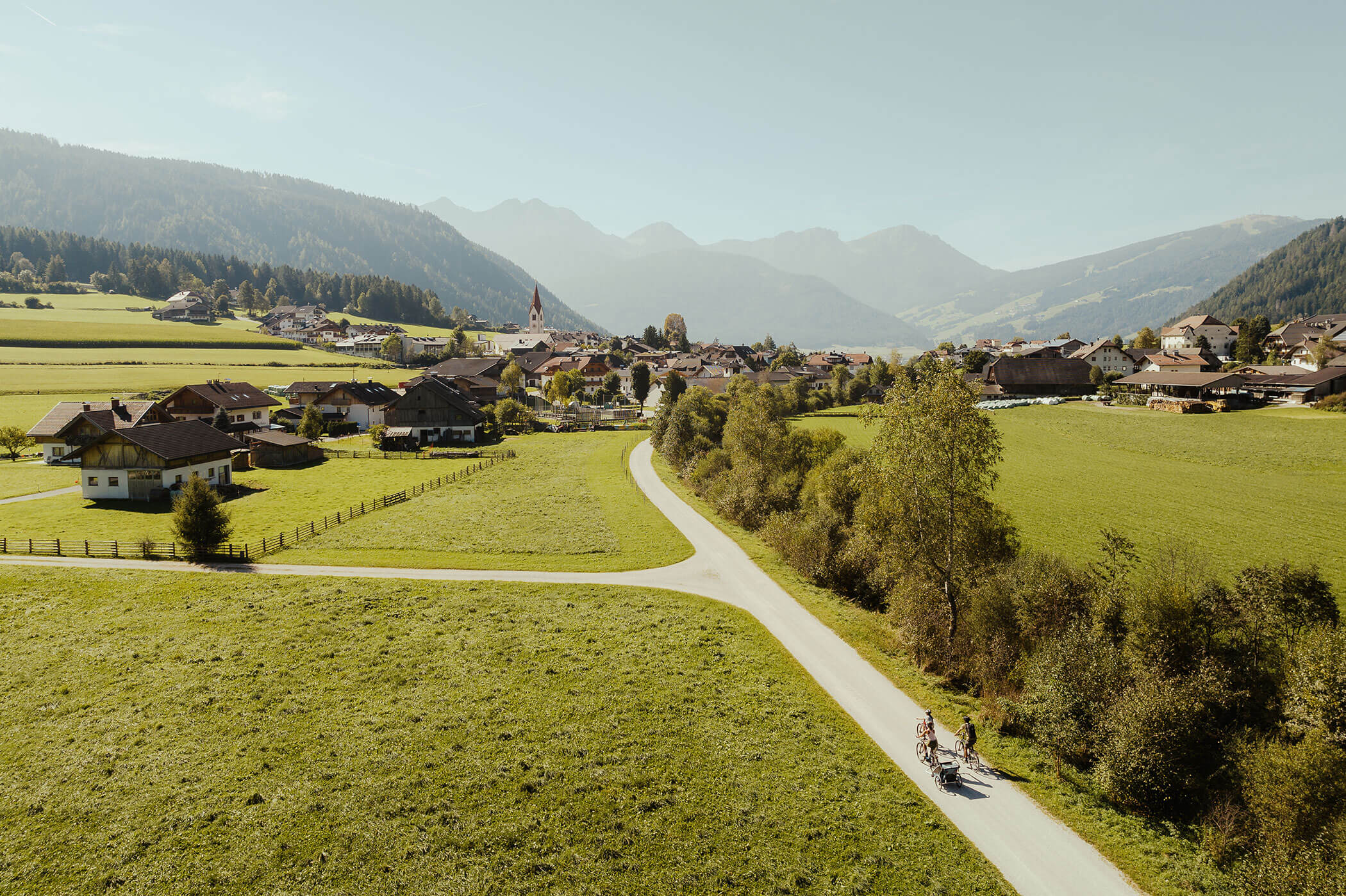 Three cyclists on a cycle path and the village of Dobbiaco in the background - Hirschenhof