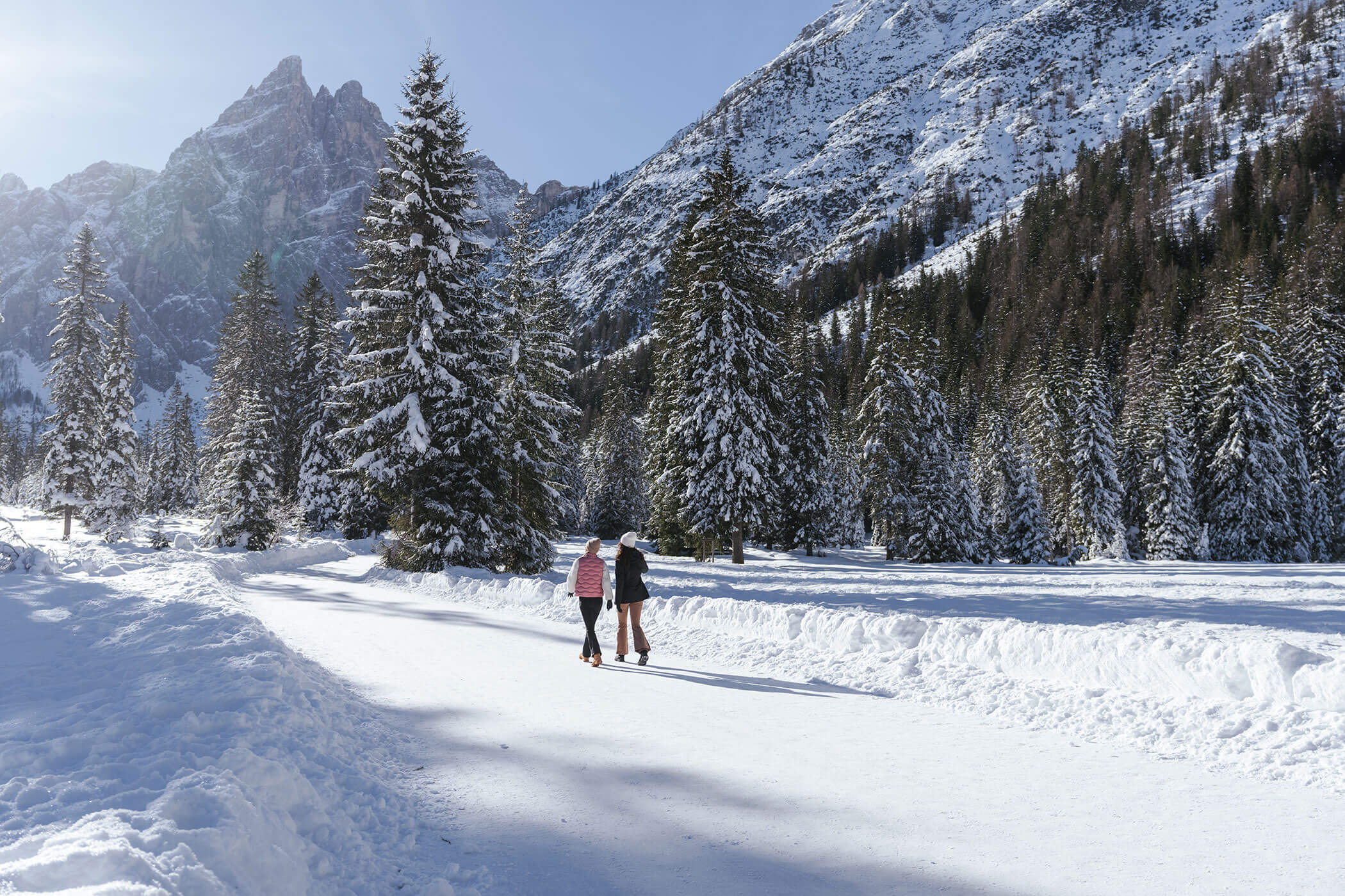 Two women hiking between the snow-covered trees and mountains - Hirschenhof